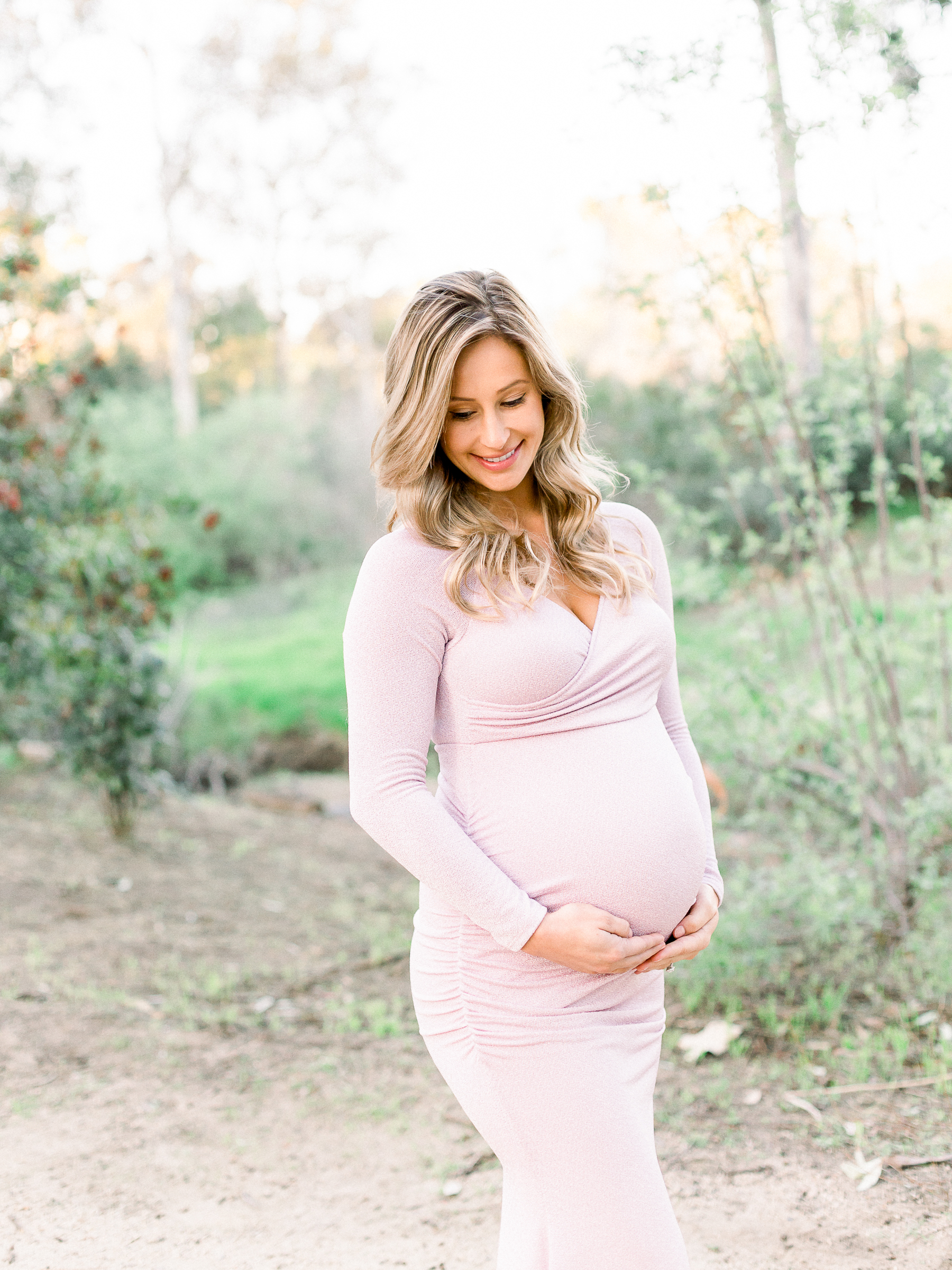 Pregnant woman smiling while holding her baby bump during her photo session