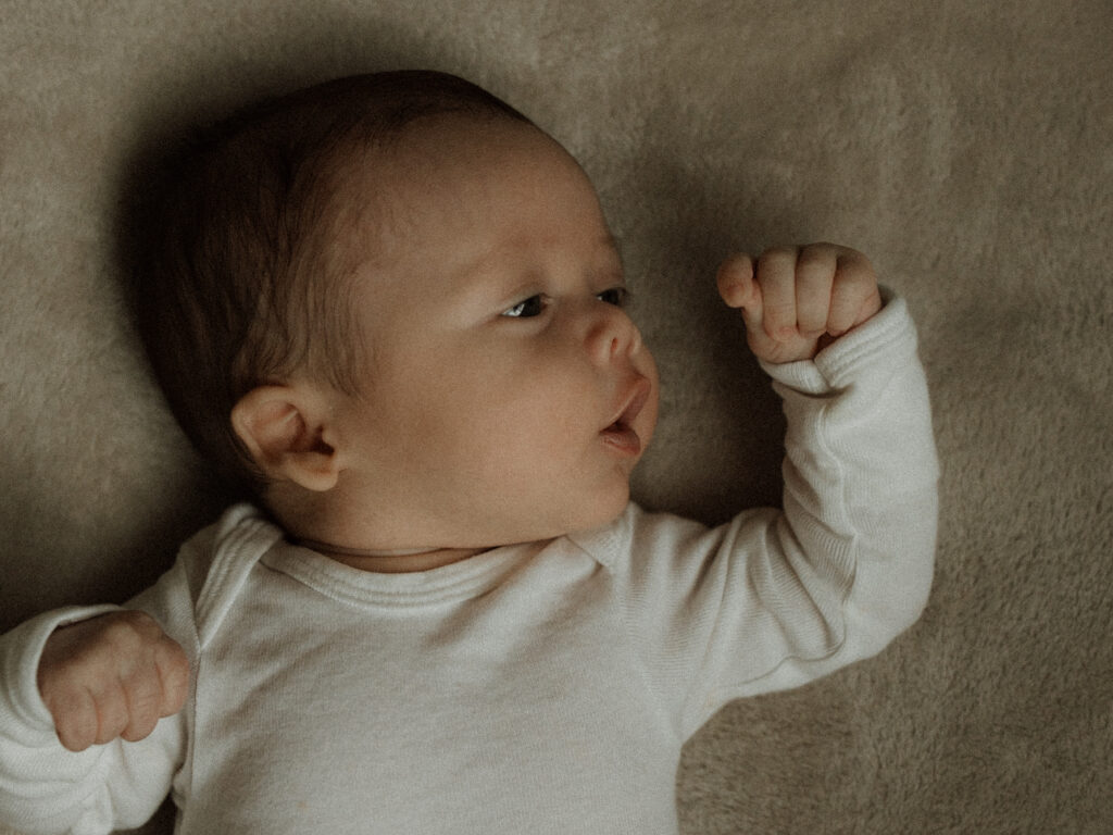 Photo of baby looking at his hand while laying on a bed.