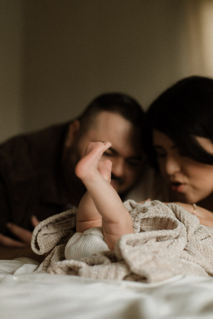 Close-up of baby's feet while laying on the bed with parents smiling.