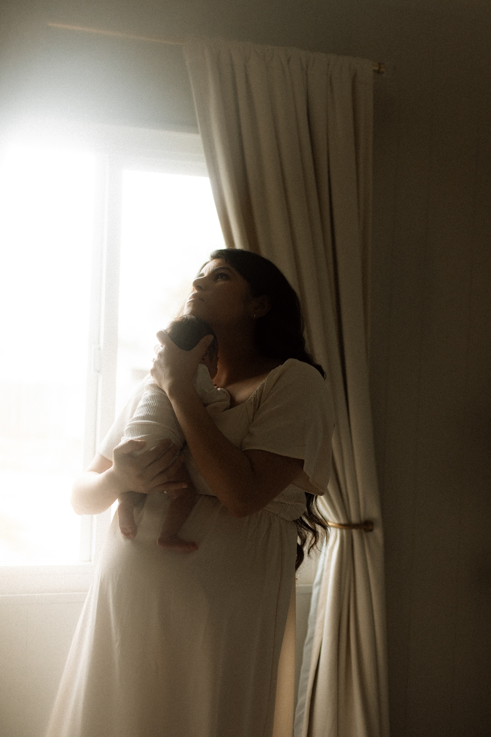 Mama gazing out the window, soft light on her face