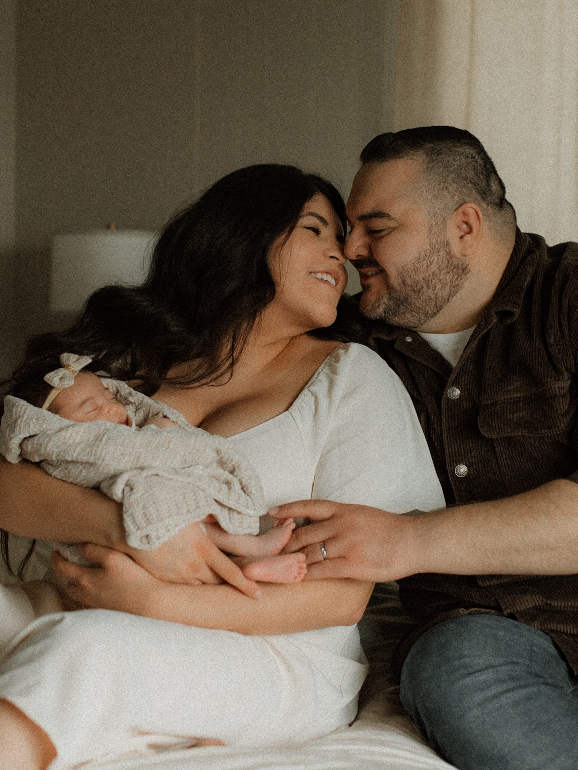 Parents sitting on the bed holding their baby girl.