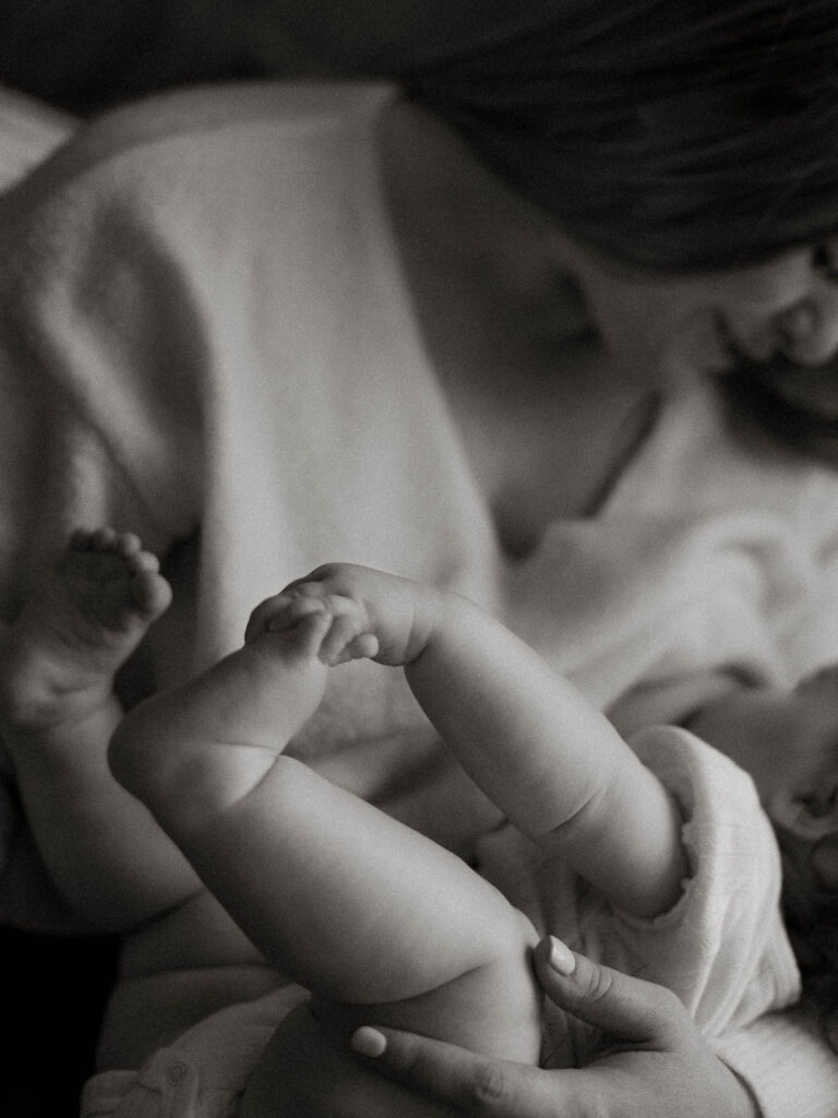 black and white of baby holding his feet while breastfeeding
